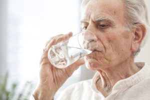 homme senior qui boit un verre d'eau contre la déshydratation en été